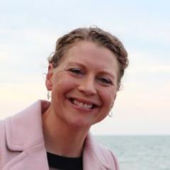 Lady looking at camera in pink jacket near beach