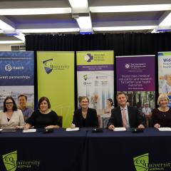 Fiver adults sitting at desk, smiling at camera