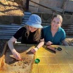 Two women sitting at table using tools to fossick through rock to find gems